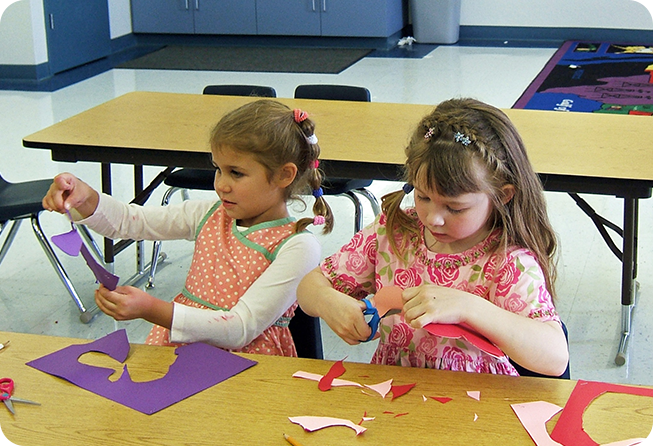 Two little girls making paper animals at a table.